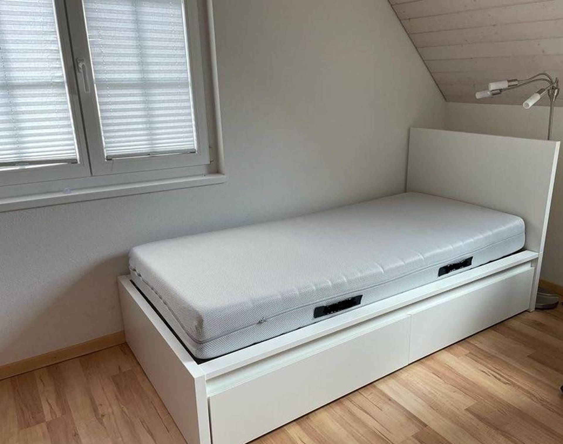 Ein weißes IKEA-Bett steht am Fenster.