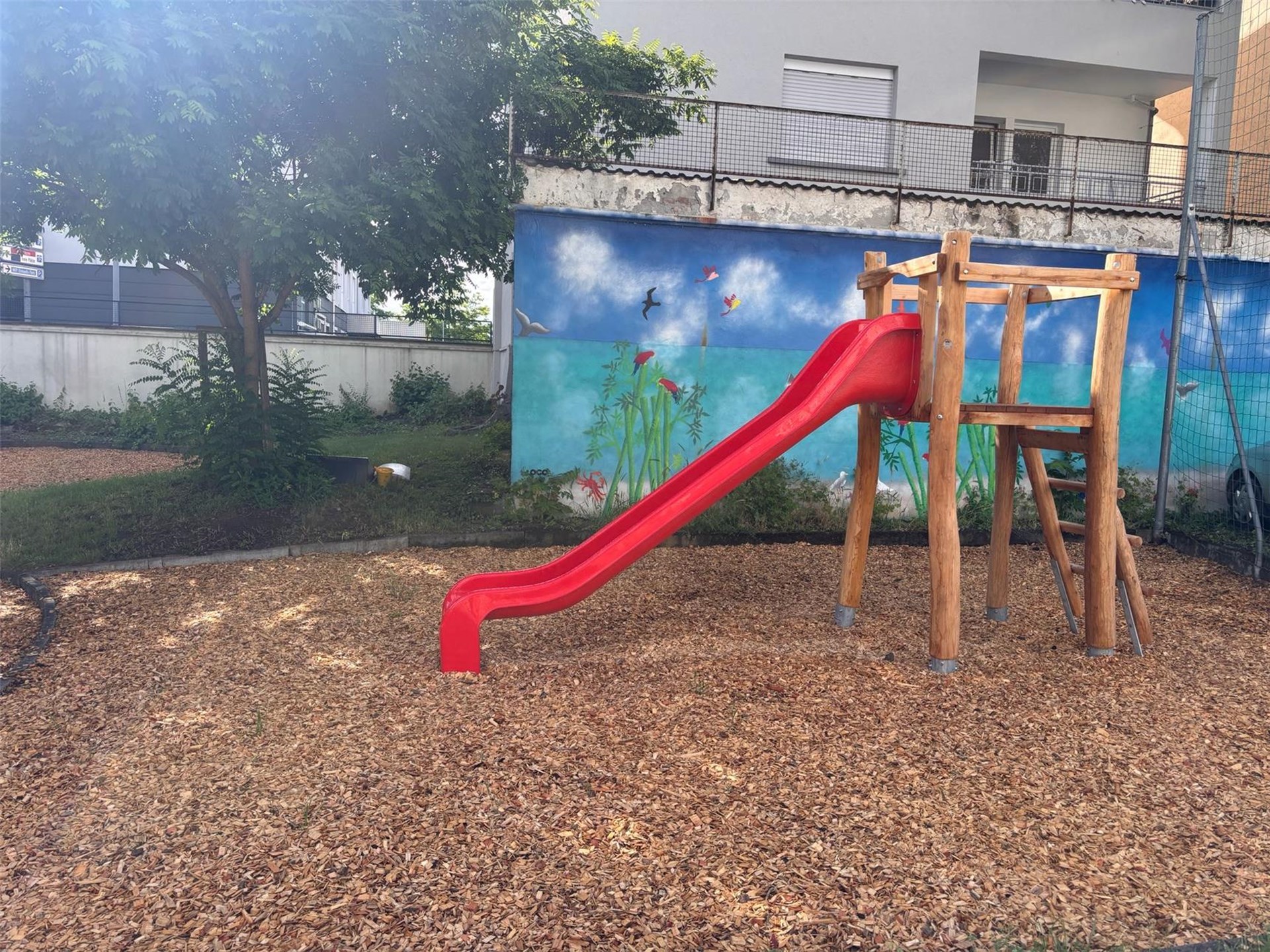 Ein Spielturm mit Leiter aus Holz und roter Rutsche steht auf einer Rindenmulch-Fläche auf dem Außengelände des Kinder- und Jugendhilfezentrums St. Marien